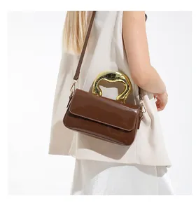 Detail of dark brown patent leather handbag with unique gold irregular metal handle