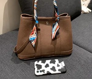 Détail d'un sac cabas en cuir marron avec poignée en soie et téléphone pour comparaison