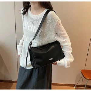 Detail of a chic black leather shoulder bag with silver logo worn by a model in casual attire