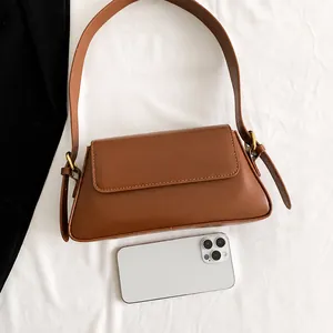 Brown faux leather baguette bag detail with adjustable strap and phone for size reference