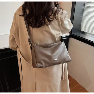 Detail of a dark brown leather crossbody bag with silver oval plaque and a wide shoulder strap