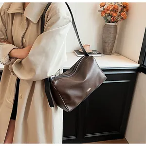 Detail of dark brown leather shoulder bag featuring a smooth matte texture and zip closure