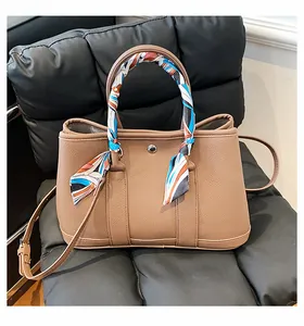 Détail du cabas en cuir grainé marron avec poignée en soie et bouton métallique
