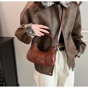 Detalle del bolso de hombro de media luna marrón oscuro con textura de cuero vintage en modelo