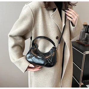 Detalle del bolso de media luna negro con textura de cuero craquelado y hebilla de metal plata