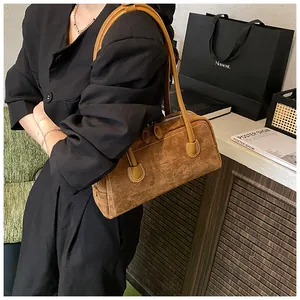 Close-up of brown suede underarm bag with decorative white stitching and top zipper