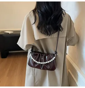 Detail of burgundy ruched crossbody bag with white pearl chain and glossy leather