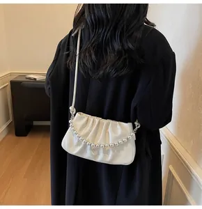 Detail of white pleated cloud bag with pearl chain shown on a model in a black coat