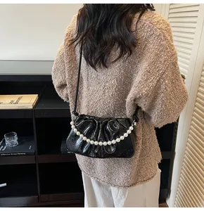 Detail of black glossy pleated cloud bag with elegant pearl chain and slim shoulder strap