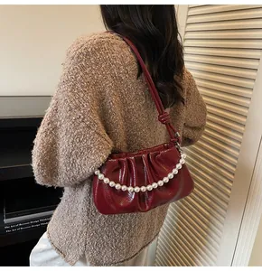 Detail of burgundy ruched cloud bag with pearl chain strap worn by a model in lifestyle setting