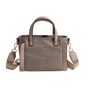 Bolso tote de nailon topo con correa ancha y remaches dorados sobre fondo blanco