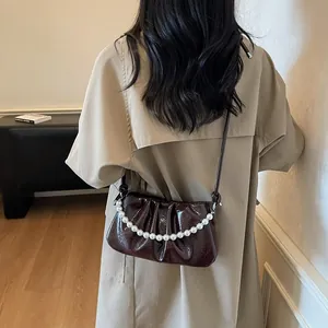 Dark red pleated leather crossbody bag with pearl chain shown on model in stylish outfit
