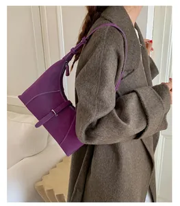 Close-up of purple suede underarm bag with white stitching and silver buckle on a model