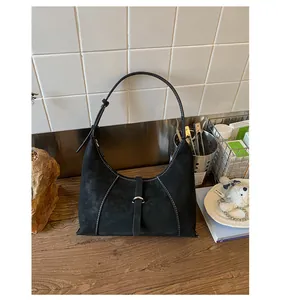 Detailed close-up of a black suede crescent bag with white contrast stitching and silver hardware