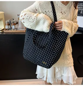 Dettaglio della grande borsa tote in tela a pois neri con targhetta metallica del logo