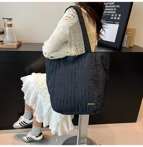 Dettaglio della borsa tote nera plissettata con tasca frontale e logo dorato da pendolare