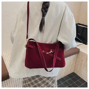 Detail of burgundy matte crossbody bag with gold hook closure on a person's shoulder