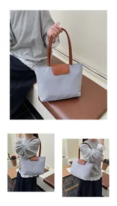 Dettaglio della borsa tote in tessuto Oxford grigio con manici in pelle marrone e logo