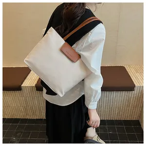 Dettaglio borsa tote in tela crema con manici in pelle marrone e logo del marchio