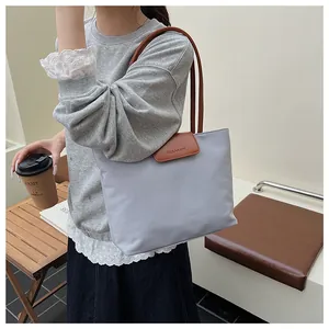 Dettaglio della borsa tote in nylon grigio con manici in pelle marrone e logo CLEARBK