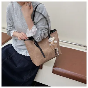 Detail of vintage embossed khaki tote bag with black straps and plush bear charm