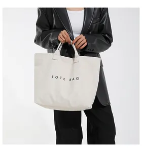 Dettaglio della borsa tote in tela color crema con scritte nere su una modella