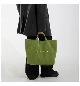 Dettaglio di una borsa tote verde con scritta TOTE BAG bianca indossata da modella