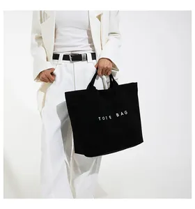 Dettaglio della borsa tote in tela nera con scritta bianca TOTE BAG sulla modella