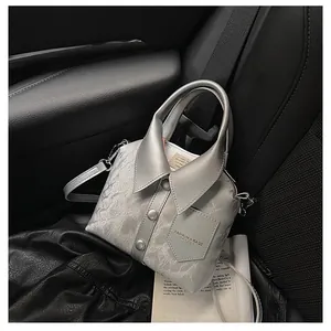 Detail of silver-grey shirt-shaped bag with collar, buttons, and shoulder strap on car seat