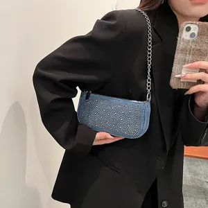 Blue denim underarm bag with silver studs and chain strap shown on a model