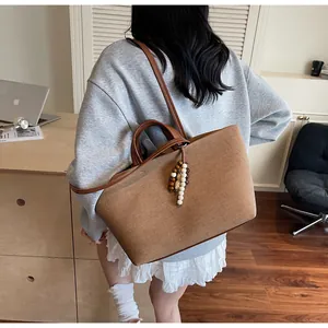 Detail of tan canvas tote bag with leather handles and wooden bead pendant on shoulder