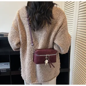 Detail of burgundy crossbody bag with suede texture and metal robot charm on sweater