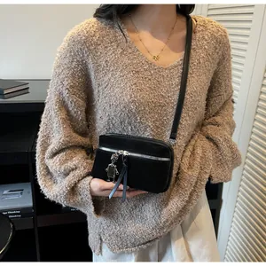 Close-up of black crossbody bag featuring silver zipper and robot charm on a knit sweater