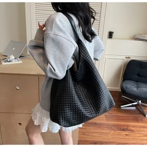 Close-up of a large black woven leather tote bag shown worn on a model's shoulder
