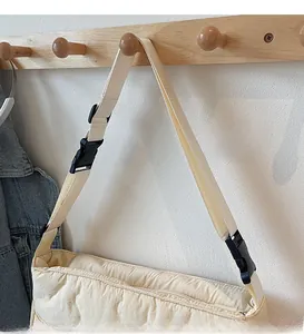 Detail of adjustable shoulder strap with buckle on a beige quilted puffer crossbody bag