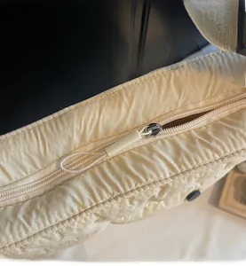 Close-up of a smooth zipper closure on a beige quilted shoulder bag with long pull tabs