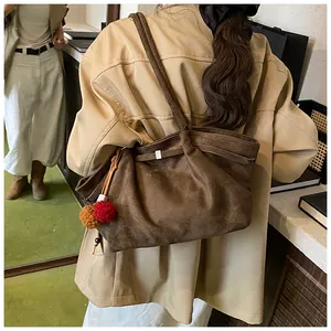Detailed view of dark brown suede tote bag featuring plush charms on a beige trench coat