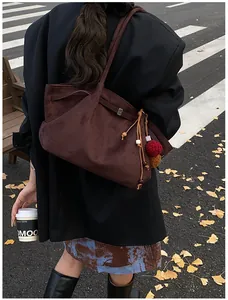 Detail of dark brown suede tote bag featuring a vintage tassel charm on the side