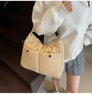 Detail of quilted beige messenger bag showing two front pockets with black snap buttons