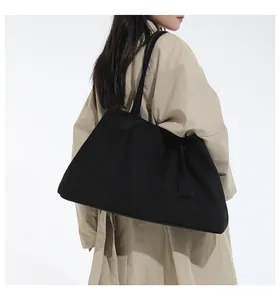 Lifestyle shot of a large black canvas tote bag worn with a beige trench coat