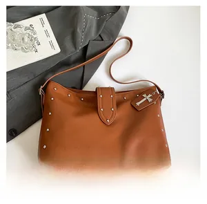 Detail van bruine leren shopper met zilveren klinknagels en kruishanger op wit decor