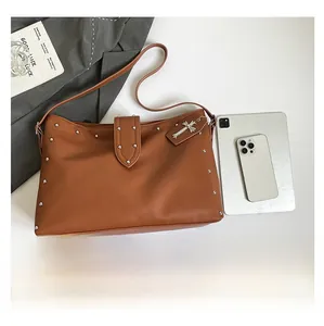 Detail van bruine leren shopper met zilveren studs en een gotische kruishanger