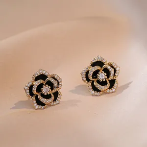 Elegantes pendientes de camelia dorados con esmalte negro y detalles de circonita blanca