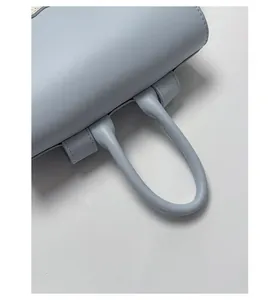 Detail of light blue leather bag with sturdy curved handle and precise stitching