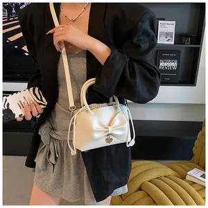 Detail of cream bucket bag featuring large bow, heart charm, and drawstring closure