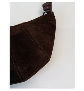 Gros plan détaillé du sac croissant en daim marron montrant les coutures et le nœud