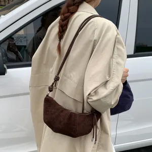 Sac croissant en daim marron foncé avec bandoulière nouée porté par un mannequin