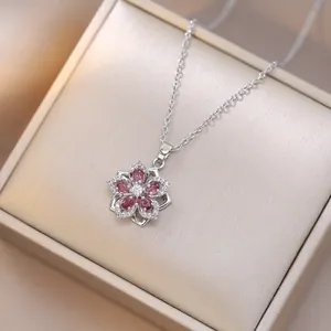 Close-up of a silver spinning flower necklace with pink zircon petals on a gift box