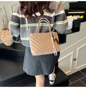 Dettaglio borsa beige con trama arricciata, ciondoli decorativi e tracolla rimovibile