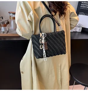 Dettaglio borsa tessuta nera con ciondoli decorativi e catena beige alla moda